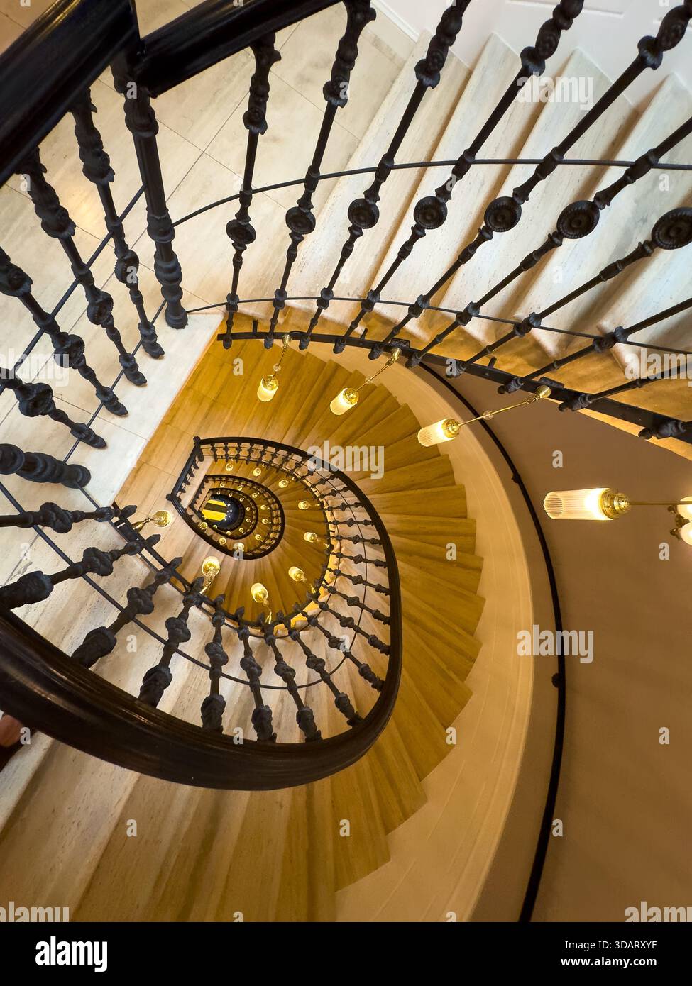 Scala a chiocciola vista dall'alto della balaustra di ferro che si snoda intorno a una calda lampadina che illumina gradini in marmo gli eleganti interni architettonici evocano un misterioso invito a esplorare Foto Stock