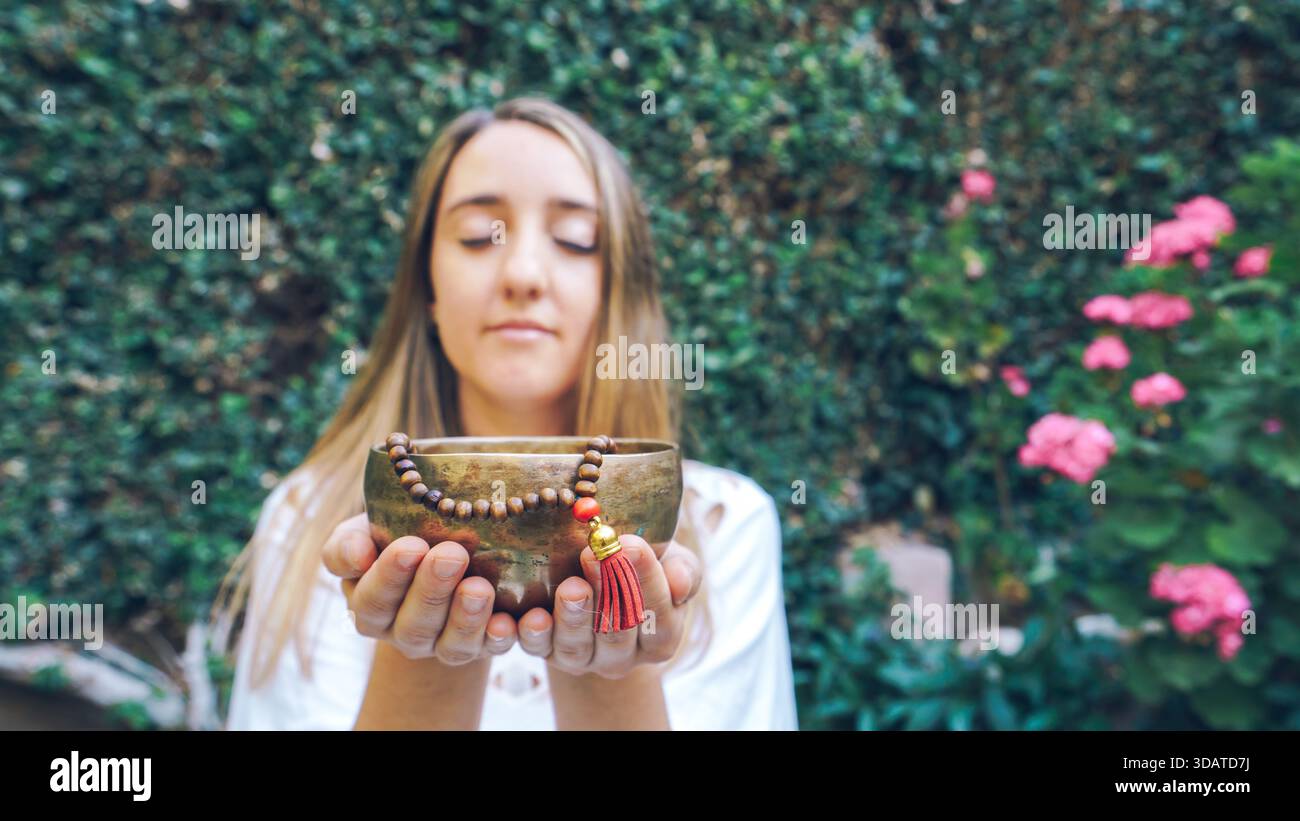 Donna che meditava con una ciotola cantante in un giardino all'aperto Foto Stock