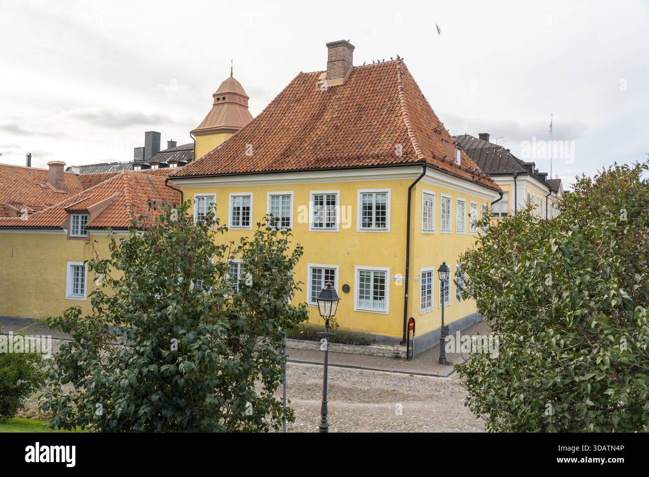 Vista di un edificio giallo con un tetto piastrellato di rosso seduto in mezzo a lussureggiante vegetazione sotto un cielo nuvoloso, Kalmar, Kalmar County, Svezia. Foto Stock