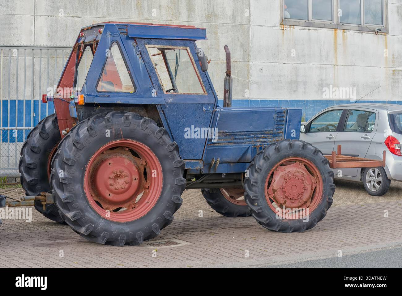 il trattore blu si trova all'esterno sulla strada accanto all'edificio di una fabbrica Foto Stock