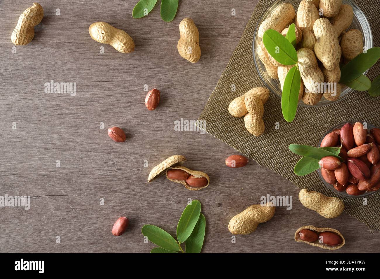 Arachidi sbucciate e non sbucciate in ciotole di vetro su una panca di legno da cucina. Vista dall'alto. Foto Stock
