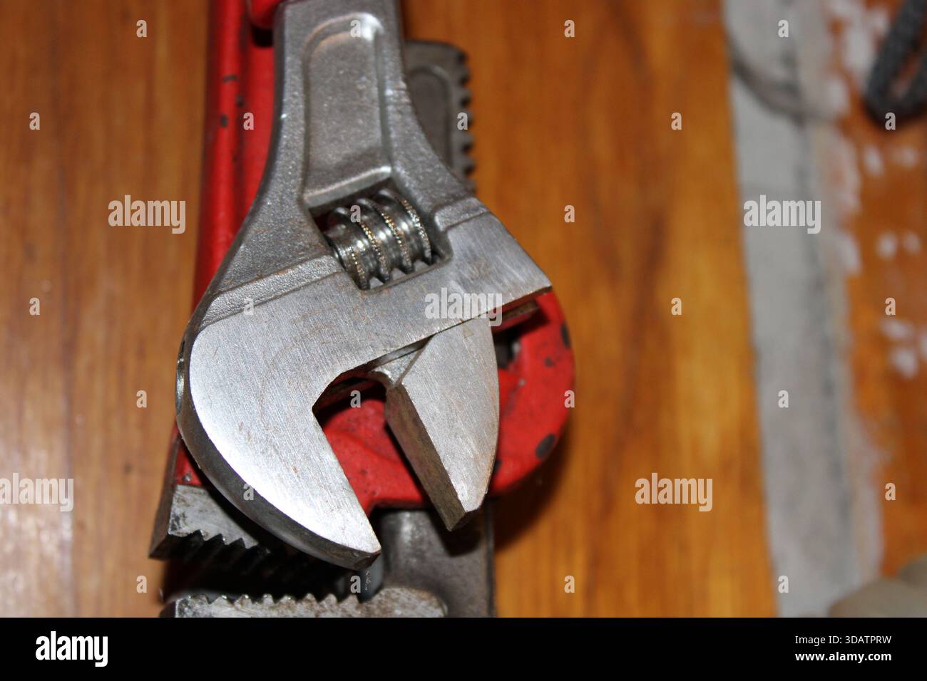 Una chiave metallica è mostrata accanto a un attrezzo di presa per tubi su una superficie di lavoro in legno. Gli attrezzi vengono utilizzati per il serraggio e l'allentamento durante le riparazioni domestiche fai da te Foto Stock