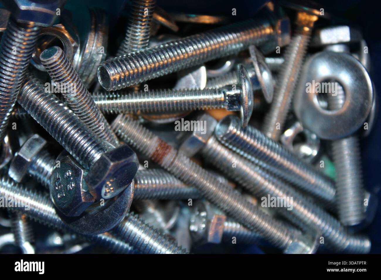 Vari bulloni e dadi in metallo vengono mescolati all'interno di un contenitore. Alcune sono lucide, altre mostrano segni di usura. Questa scena è comune nella costruzione o nella REP Foto Stock