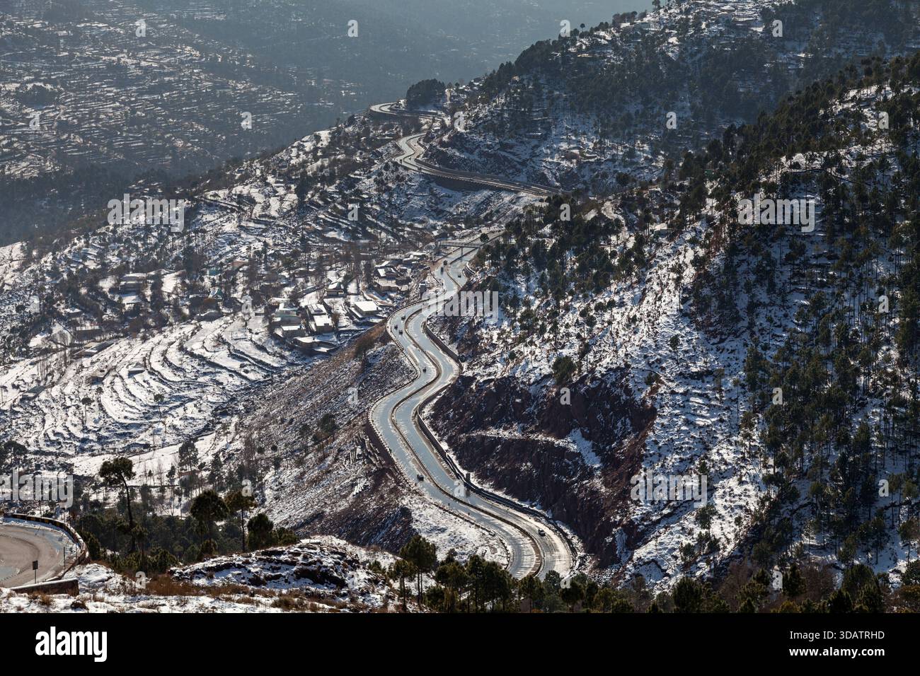Vista di una strada tortuosa che serpeggia attraverso colline innevate, un nastro aspro in asfalto che contrasta con il paesaggio bianco incontaminato, Murree, Punjab, Pakista Foto Stock