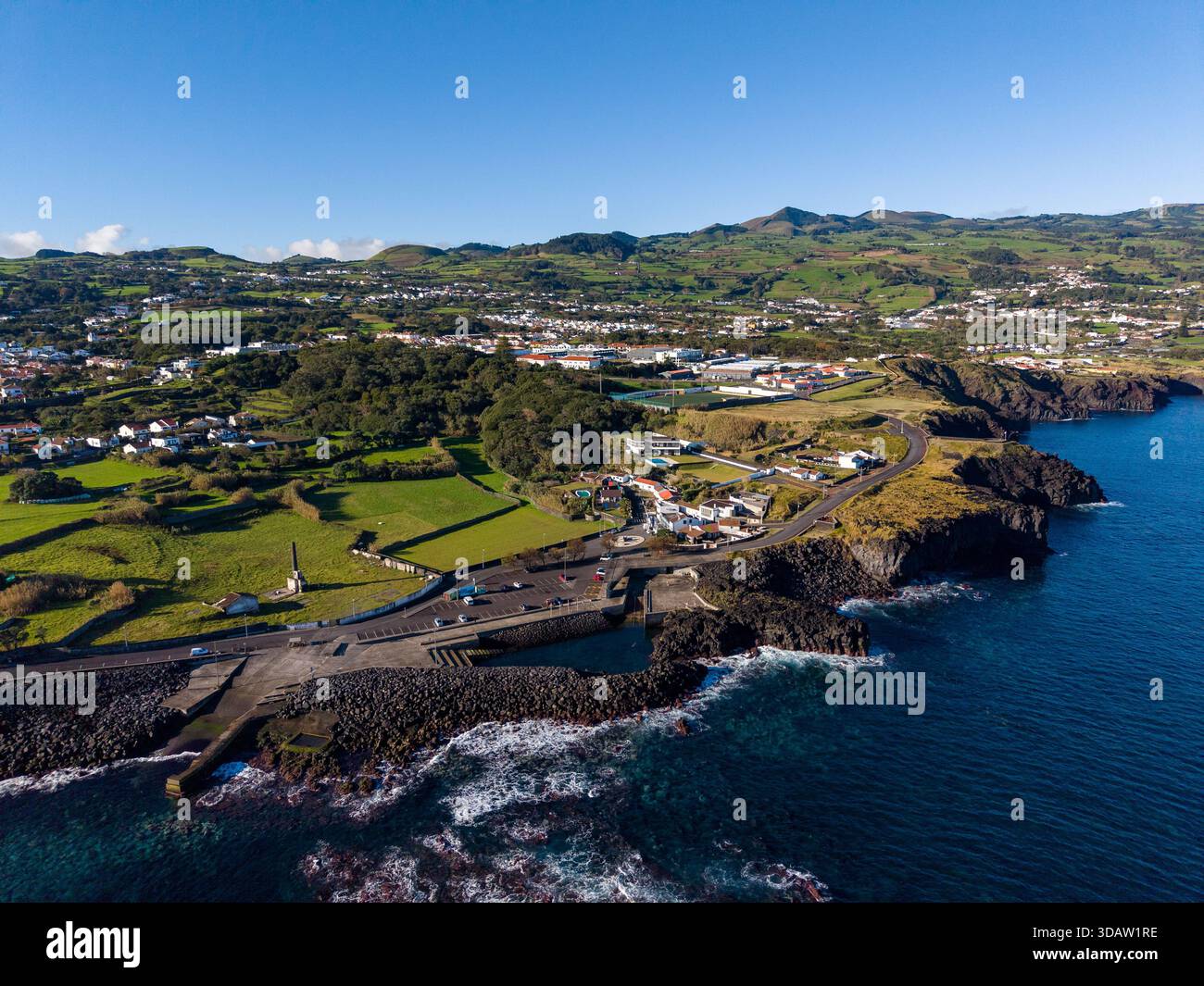 Vista aerea della costa frastagliata che incontra il mare blu profondo, contrastando con le verdi colline verdeggianti e il pittoresco villaggio di Capelas, Azzorre, Portu Foto Stock