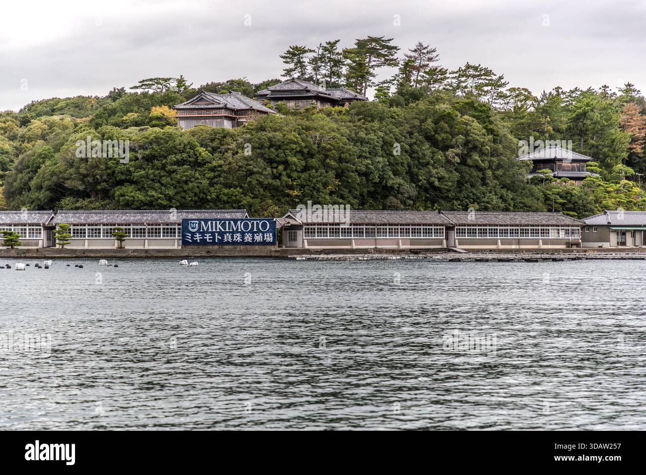 Gli edifici tradizionali in legno della fattoria di perle Mikimoto costeggiano la riva della baia di Ago, visti qui dall'acqua. Shima, Prefettura di Mie, Giappone. Foto Stock