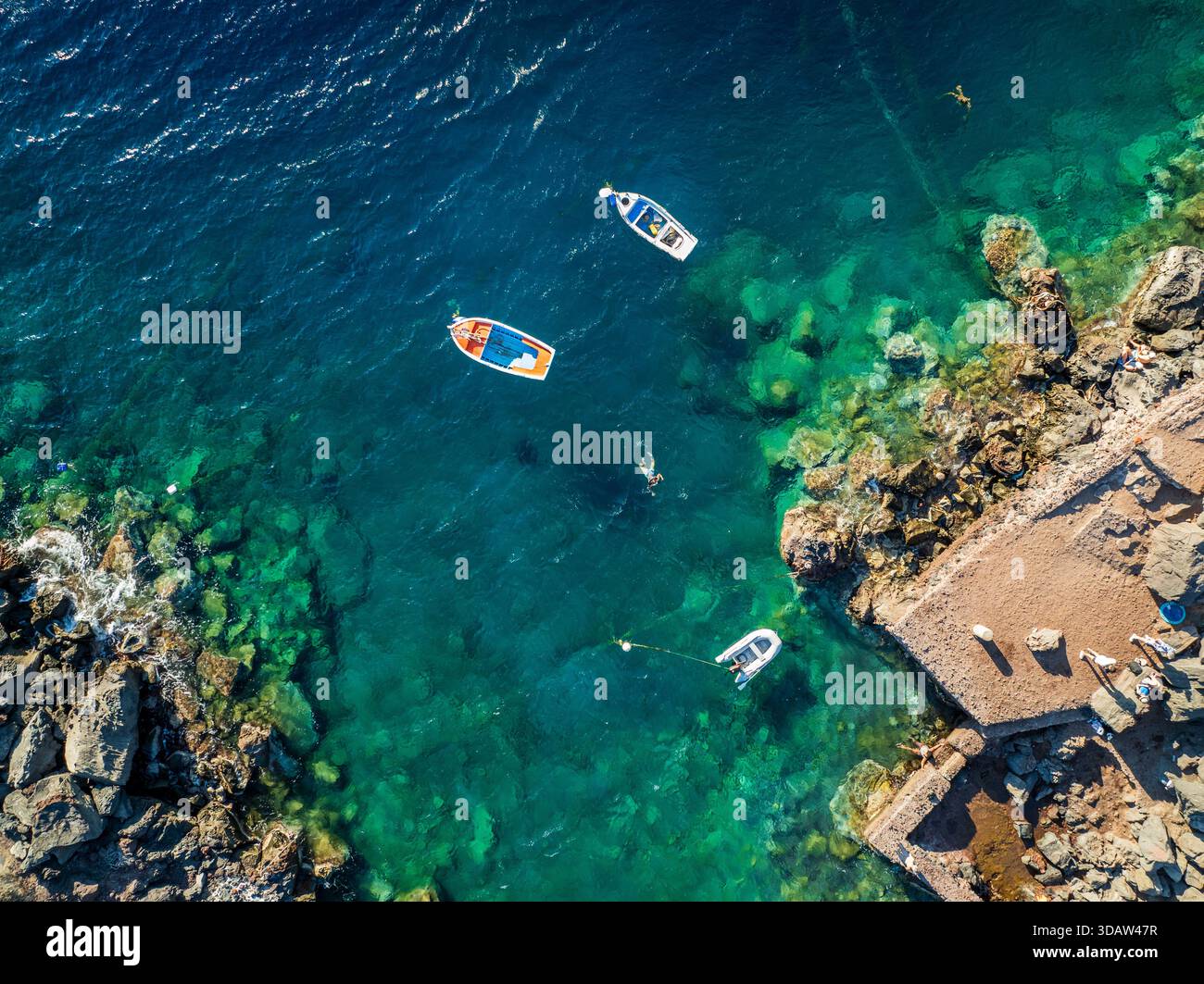 Vista aerea delle barche che si stagliano nelle acque turchesi vicino alla costa rocciosa e alle strutture in pietra, un'affascinante miscela di bellezza naturale e artificiale Foto Stock