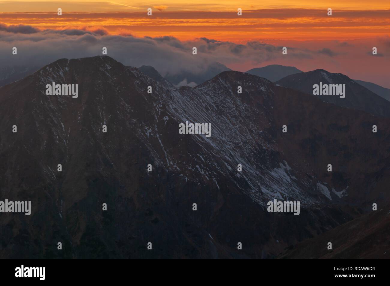 Vista aerea delle aspre cime innevate dei Tatra occidentali sotto un tramonto ardente, nuvole aggrappate alle alture, da Bystra, regione di Zilina, S. Foto Stock