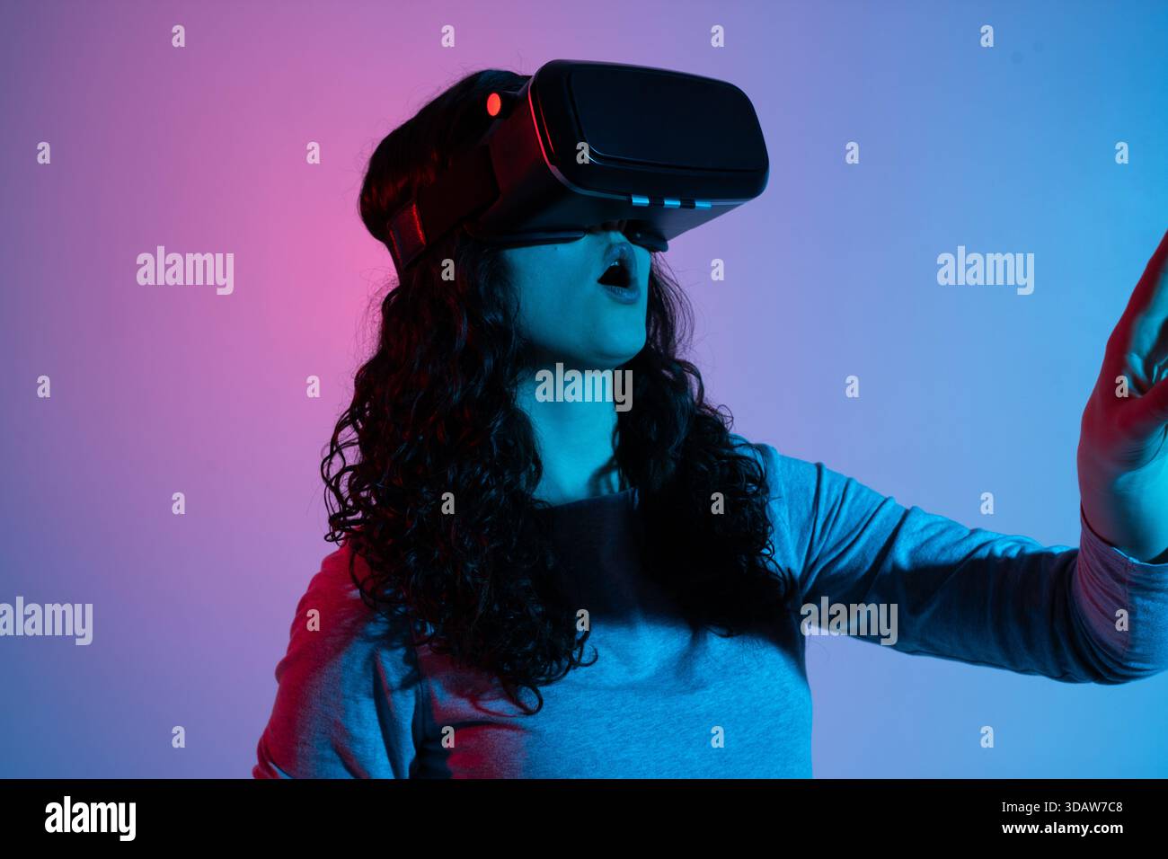 Donna che reagisce ai contenuti di realtà virtuale indossando un visore VR con luci rosse al neon e blu a contrasto Foto Stock