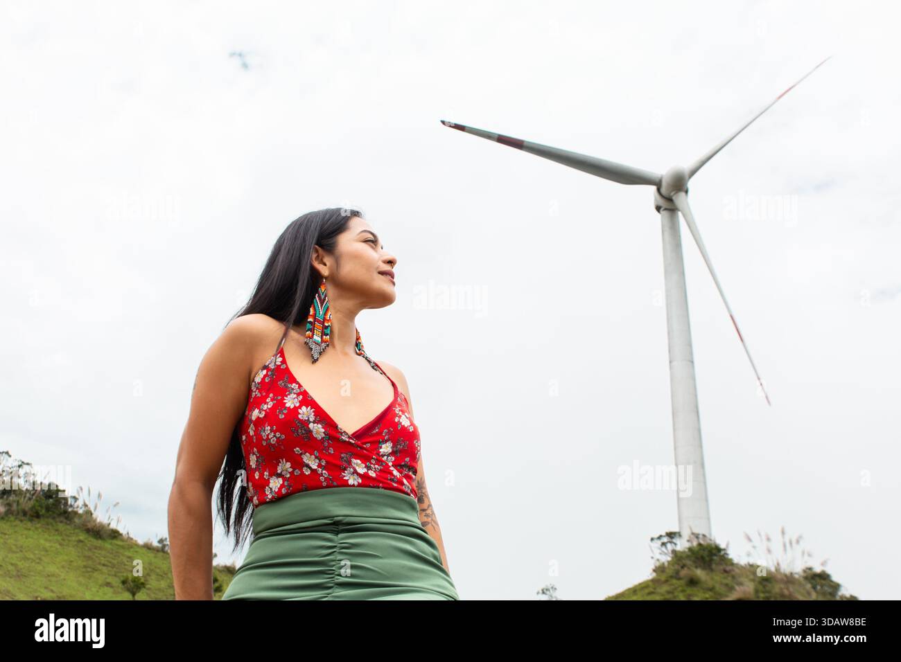 Una donna si trova di fronte a una torreggiante turbina eolica, a simboleggiare l'armonia tra tecnologia e natura. La scena cattura lo spirito di Sustainabl Foto Stock