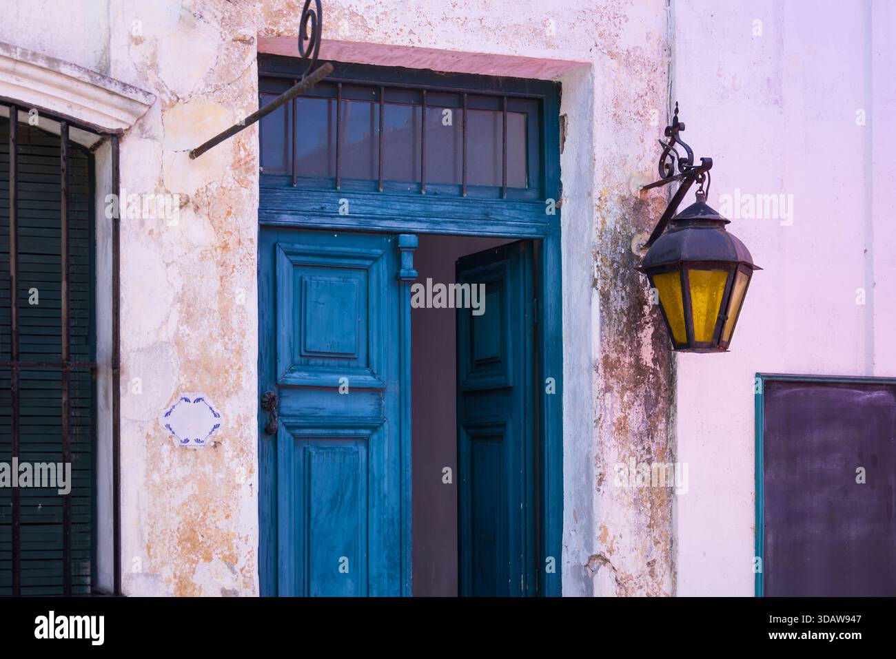 Una porta in legno blu vibrante con una lanterna rustica adorna un vecchio muro testurizzato a Colonia del Sacramento, Uruguay, che mostra l'affascinante colon della città Foto Stock