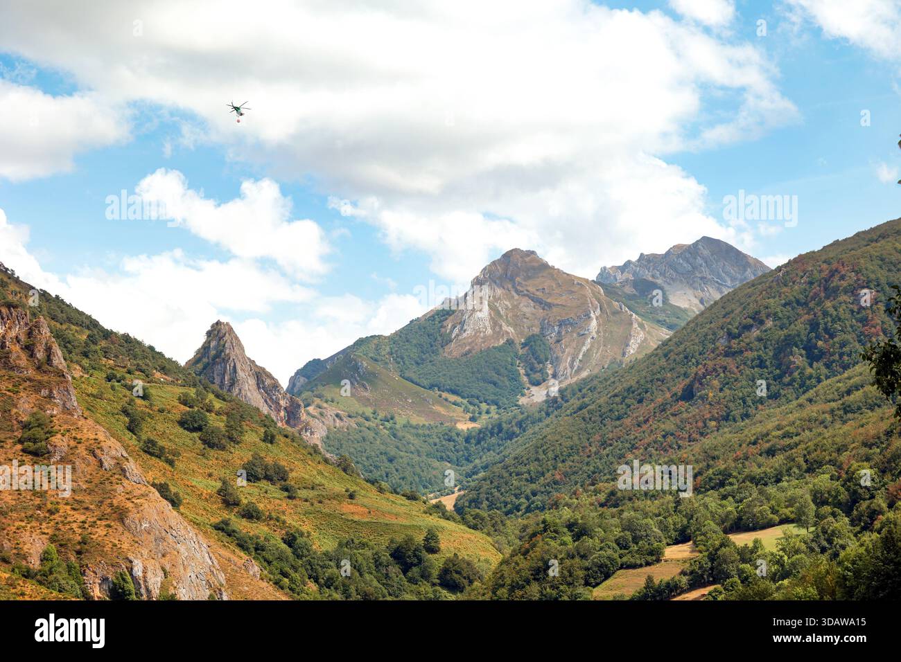 Nei cieli sopra la Valle de Somiedo, un elicottero affronta un incendio boschivo, mettendo in evidenza gli sforzi urgenti per proteggere la vegetazione lussureggiante e la natura Foto Stock