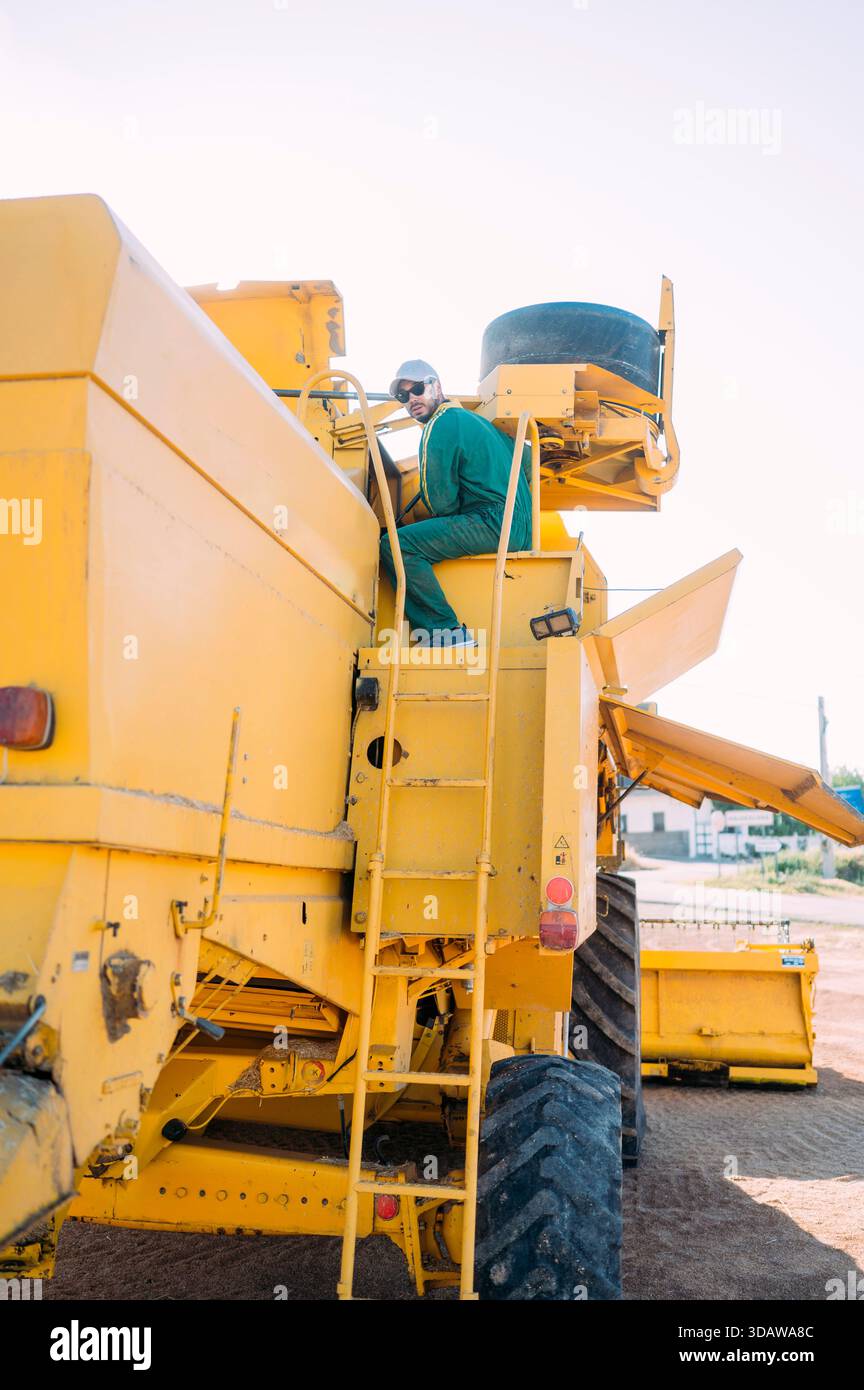 Un agricoltore gestisce una grande macchina agricola gialla contro un cielo limpido a Guadalajara, in Spagna, mostrando le moderne tecnologie e attrezzature agricole Foto Stock