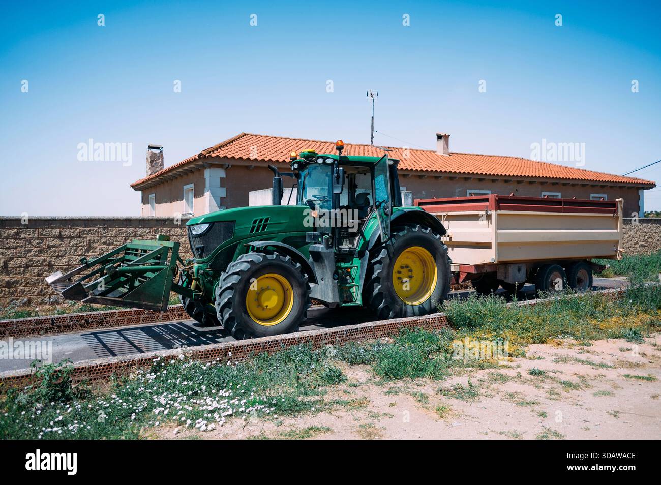 Un trattore verde con un grande rimorchio parcheggiato in un'azienda agricola di Guadalajara, Spagna. L'ambiente agricolo mette in risalto il fascino rustico della tradizione Foto Stock