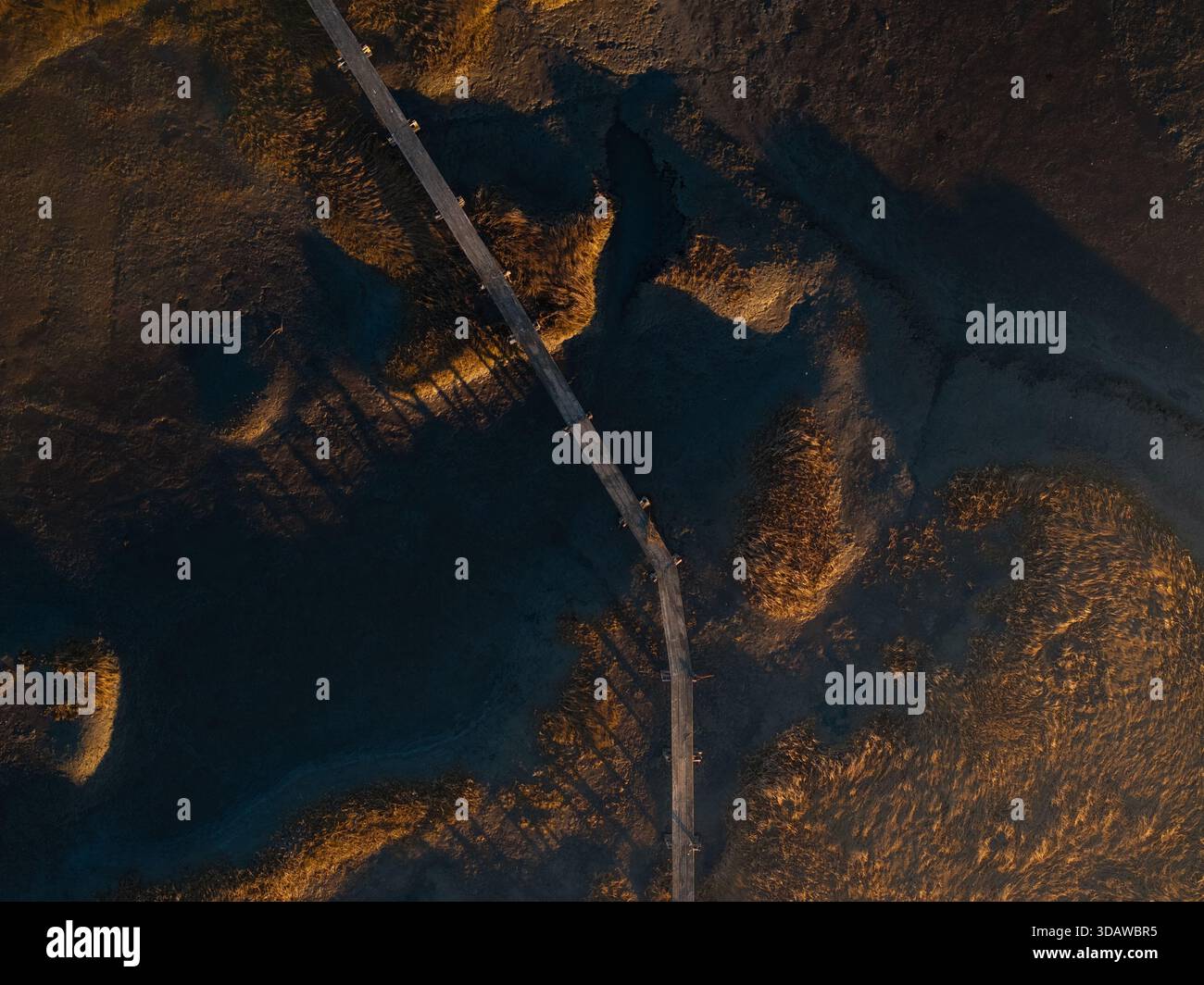 Vista aerea di una passerella di legno che attraversa il paesaggio scuro e paludoso, contrastando nettamente con le tonalità dorate del sole che tramonta, Gloucester, Foto Stock