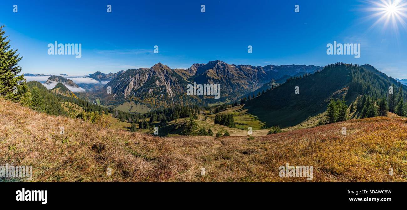 Una vista panoramica cattura una tranquilla escursione autunnale attraverso pittoresche montagne, con vegetazione lussureggiante e fogliame dorato sotto la luce del sole nell'Allga Foto Stock