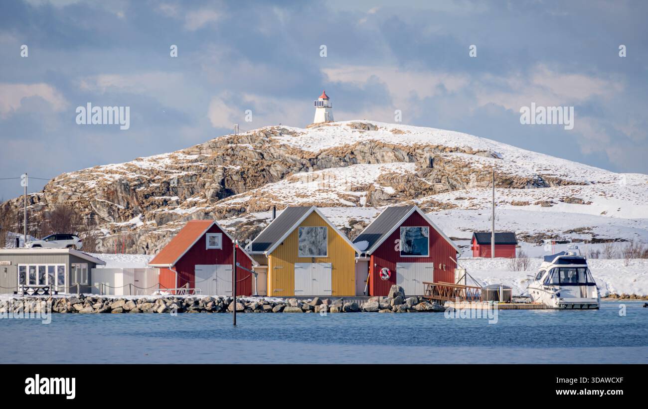 Una tranquilla vista di case colorate e un faro in cima alle colline innevate di Sommaroy, sulla costa norvegese, catturando l'essenza della pacifica Scandina Foto Stock
