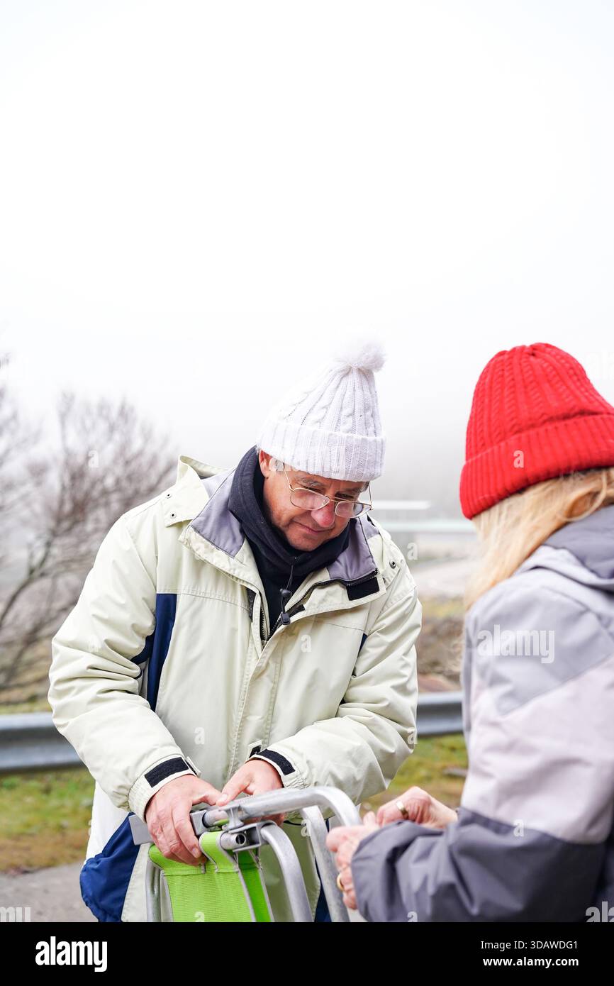 Una coppia più anziana si è impegnata in attività invernali, godendosi il freddo all'aperto. Sono vestiti con calore con cappotti e cappelli a maglia, che incarnano gioia e. Foto Stock