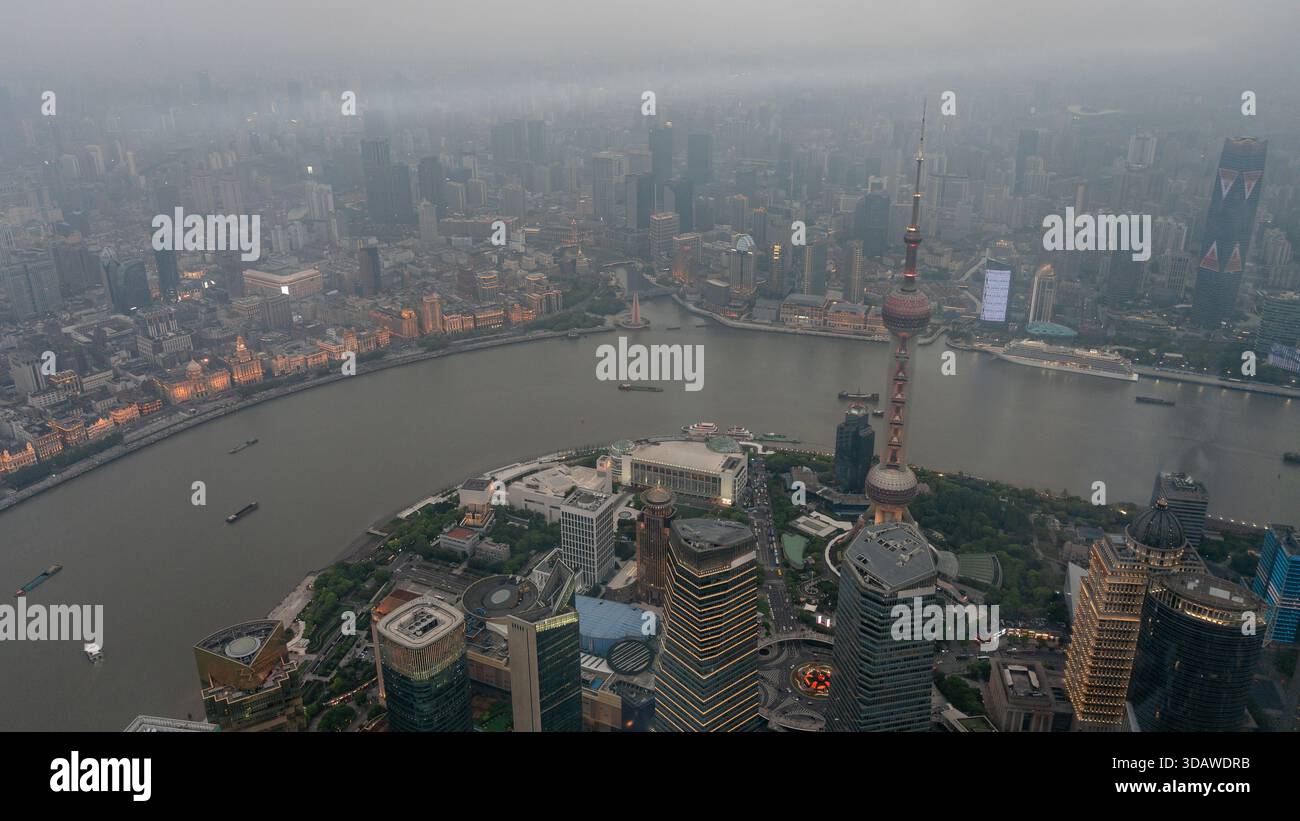 Vista aerea mozzafiato di Shanghai, Cina, con iconici grattacieli, il sereno fiume Huangpu e un vivace paesaggio urbano sotto un cielo nebbioso. Foto Stock