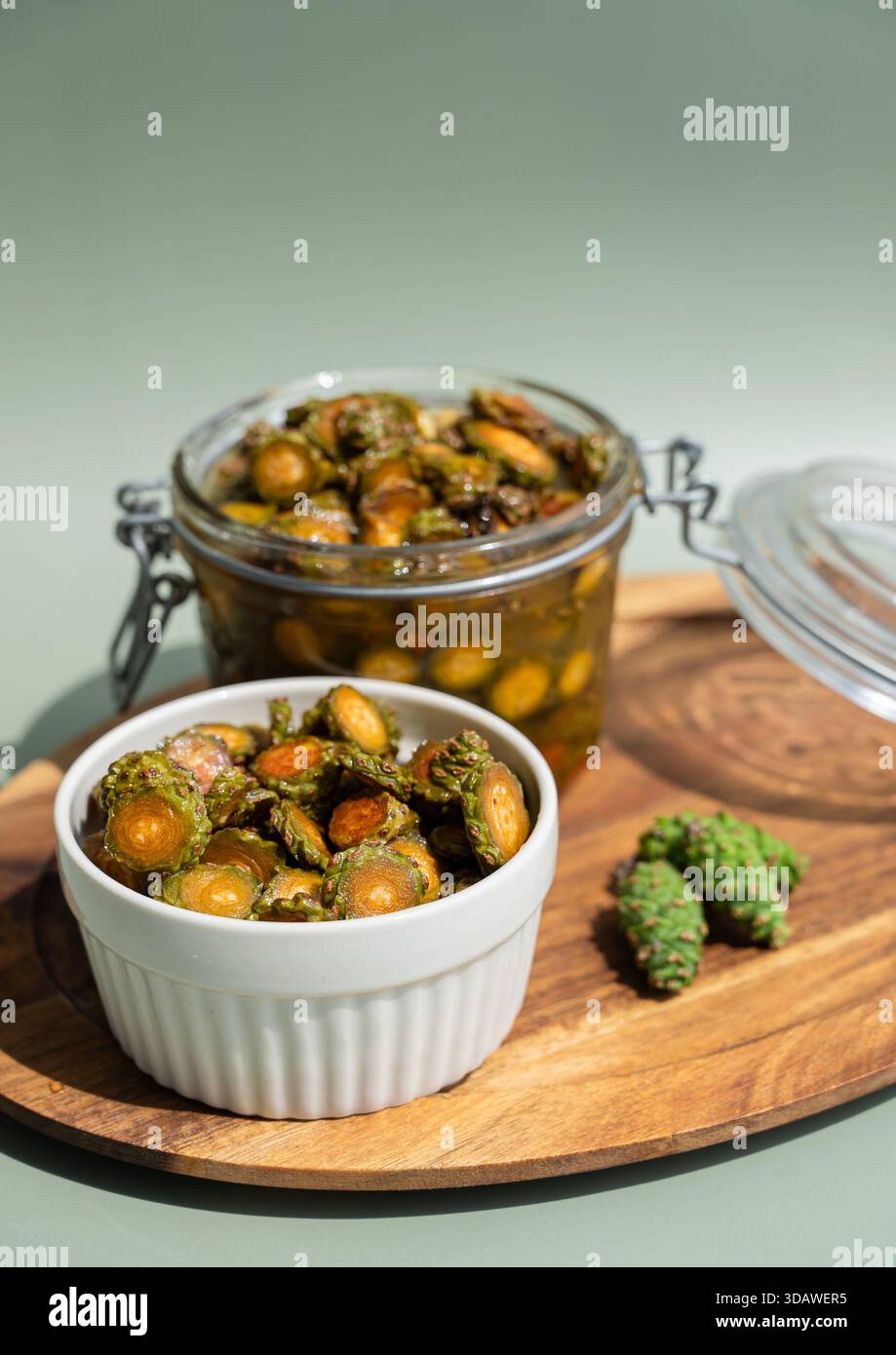 Primo piano di miele di cono di pino biologico in un recipiente di ceramica bianca e vaso di vetro trasparente su un vassoio di legno Lo sfondo verde naturale migliora il rustico p Foto Stock