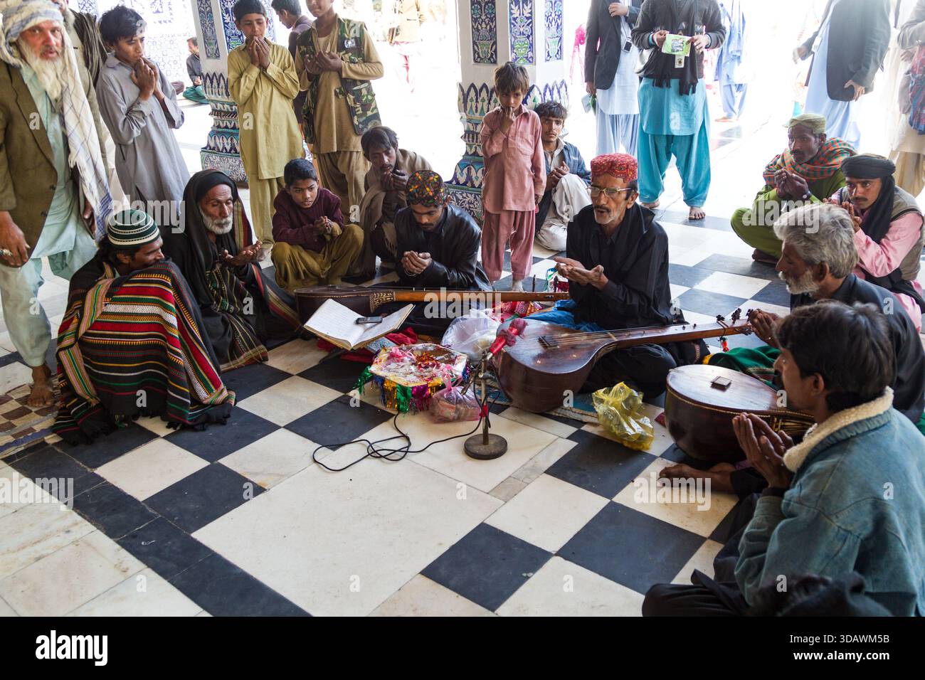 Bhit Shah, Pakistan - 5 dicembre 2025: Veduta dei musicisti riuniti in cerchio, i loro strumenti riflettono la luce contro il til bianco e nero Foto Stock