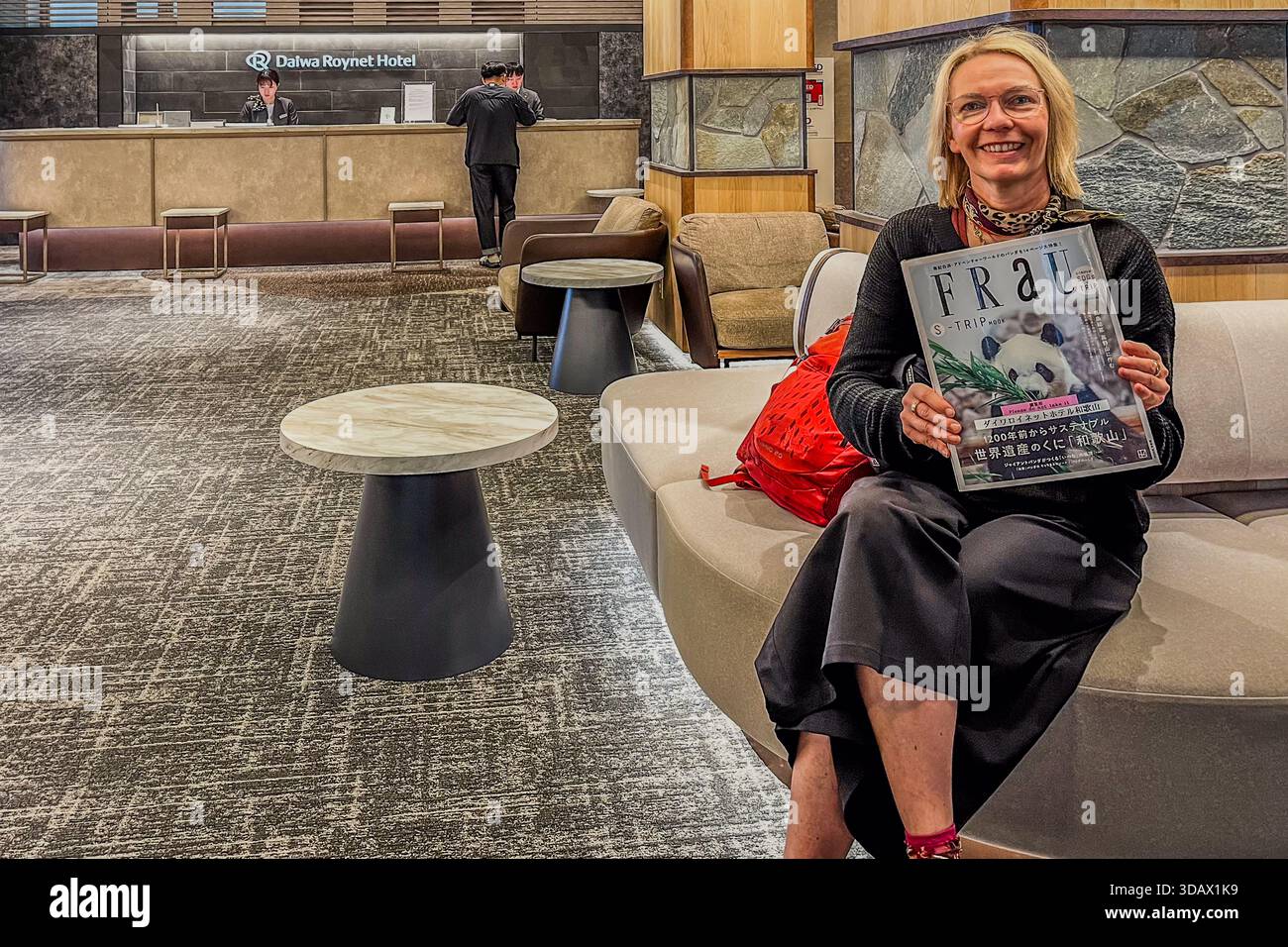 Angela Berg è seduta sorridente su un divano nella hall del Daiwa Roynet Hotel Wakayama, in Giappone, tenendo in mano una copia della rivista giapponese di lifestyle "FRAU" con un panda in copertina. Il titolo, tedesco per "donna", è stato scelto all'inizio degli anni '90 per evocare un'immagine intellettuale ed europea, e la rivista si rivolge a donne tra la metà dei vent'anni e l'inizio dei trent'anni; questo numero presenta la prefettura di Wakayama come destinazione di viaggio sostenibile. Foto Stock
