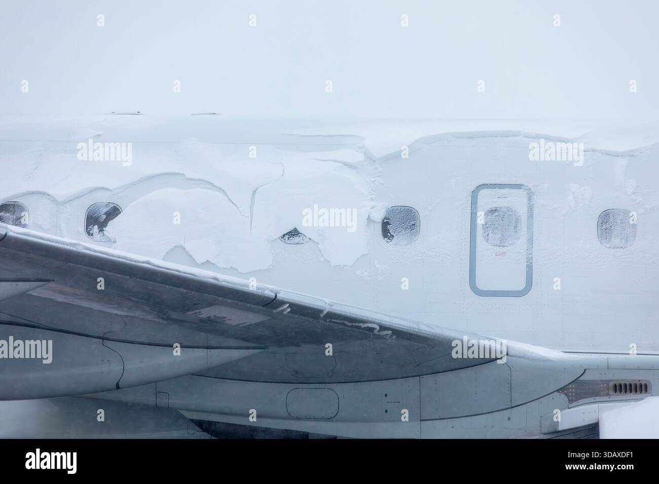 I finestrini innevati dell'aeroplano attendono lo sbrinamento durante le fredde giornate invernali all'aeroporto. La scena mostra le condizioni di gelo sulla superficie dell'aereo creando la tipica i Foto Stock
