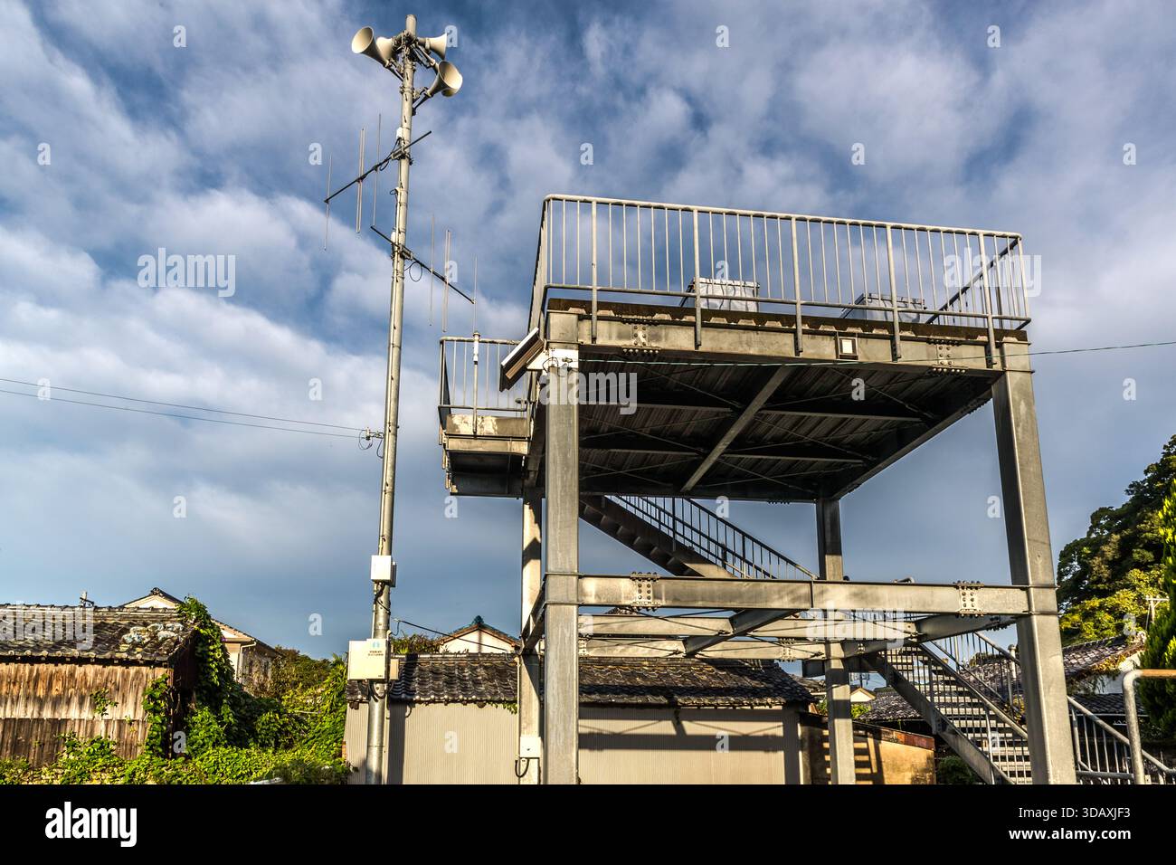 Un masto di sirena e la piattaforma di osservazione della torre di evacuazione per gli tsunami si innalzano sopra le case di Nachikatsuura, prefettura di Wakayama, Giappone. La città si trova sulla costa del Pacifico in una regione che sarebbe colpita da un’onda tsunami in caso di terremoto nel fossato di Nankai. Foto Stock