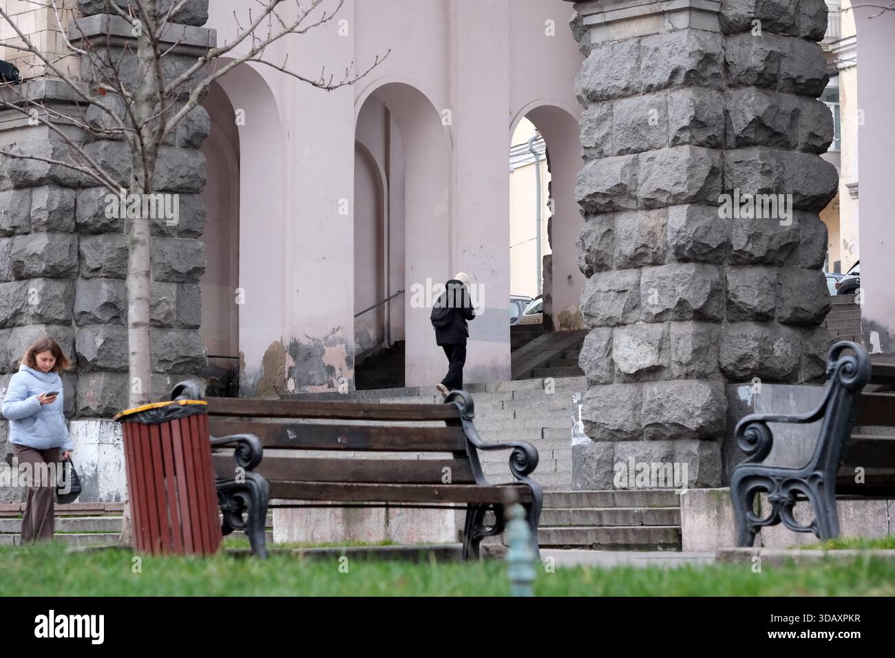 Una persona si allontana sotto grandi archi di pietra mentre un'altra guarda il telefono. Kiev, Ucraina. 12 dicembre 2025. Foto Stock