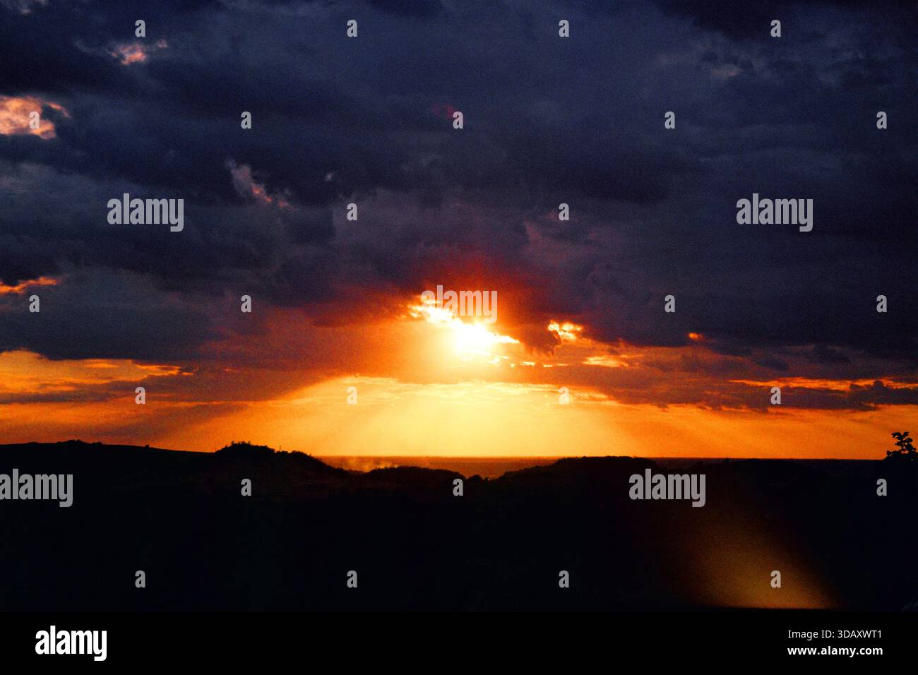 Sole basso che si infrangono tra le nuvole sopra colline e pianure sagomate, riflessi dell'obiettivo, colori analogici ricchi, intramontabile scena cinematografica da 35 mm. Foto Stock