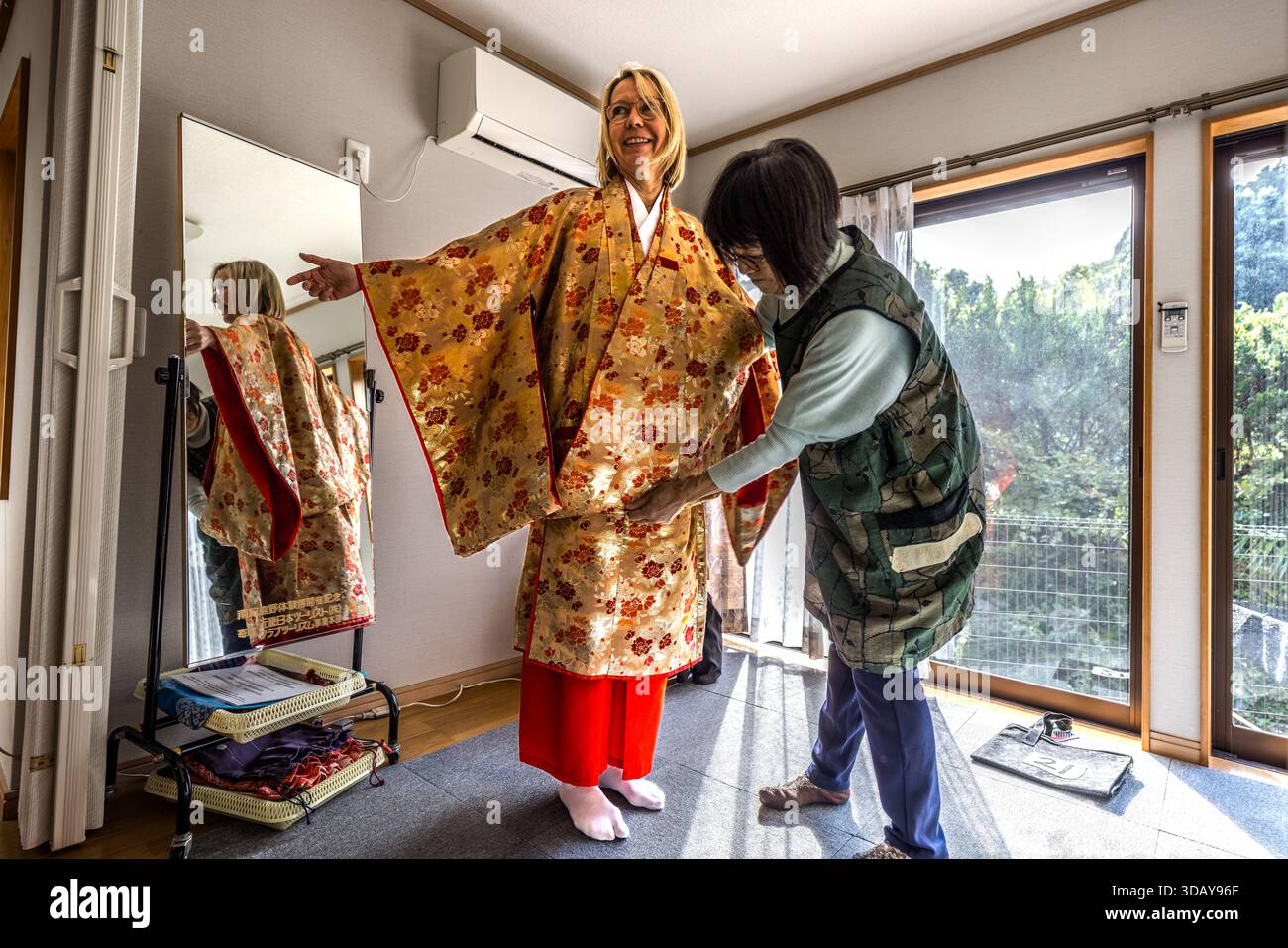Un turista prova un kimono noleggiato a Nachikatsuura, prefettura di Wakayama, Giappone. Il personale di un negozio di noleggio in stile Heian adatta il kimono dorato alla sua taglia prima che lei si imbarchi su una parte del percorso di pellegrinaggio Kumano Kodo. Foto Stock