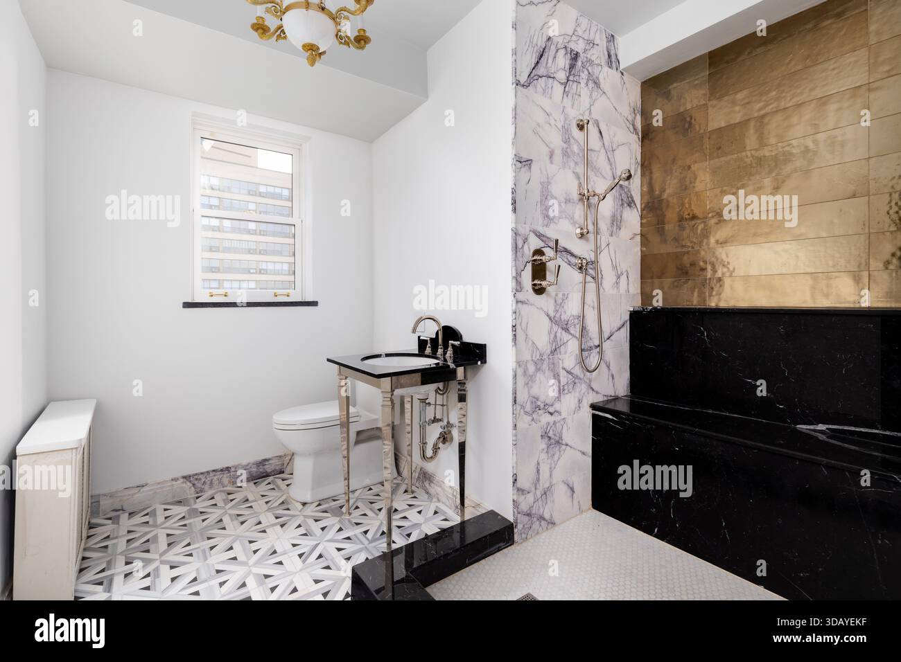Un lussuoso bagno moderno con un'elegante panca per doccia nera, pareti in marmo calacatta e piastrelle dorate, lavandino e lampadario a consolle dorate. Foto Stock