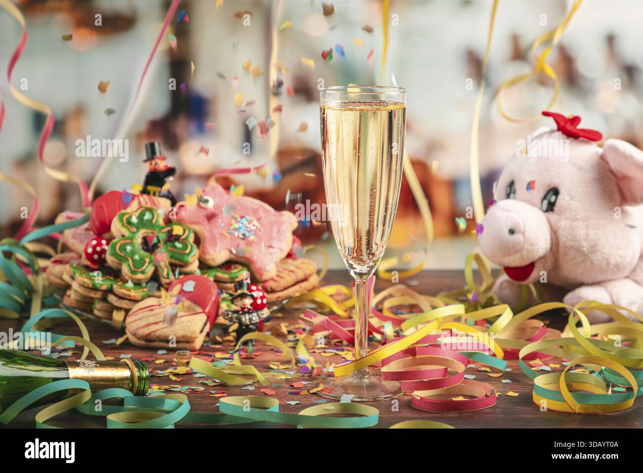 Coriandoli cadenti su un bicchiere di champagne circondato da biscotti di Capodanno, rastrellini e maiale di peluche Foto Stock
