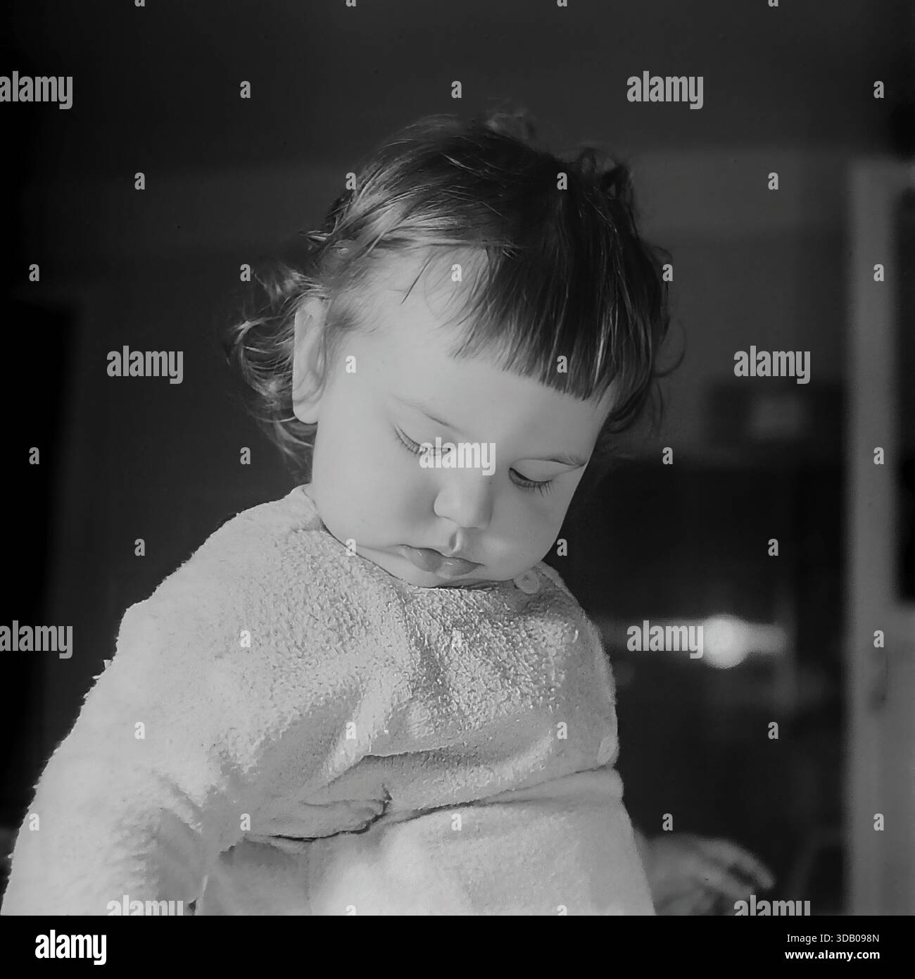 Slavyansk, Ucraina, URSS. Un toccante ritratto d'archivio degli anni '1960 che cattura un momento tranquillo di un bambino in casa. Il simpatico bambino, vestito con una morbida camicia testurizzata, guarda verso il basso con un'espressione timida e modesta, abbassando gli occhi. La spettacolare retroilluminazione mette in risalto i suoi capelli, creando un effetto alone sullo sfondo scuro. L'immagine in bianco e nero trasmette innocenza, tranquillità e l'atmosfera di un'infanzia felice nella tranquilla città industriale di Donbass durante l'era del disgelo. Foto Stock