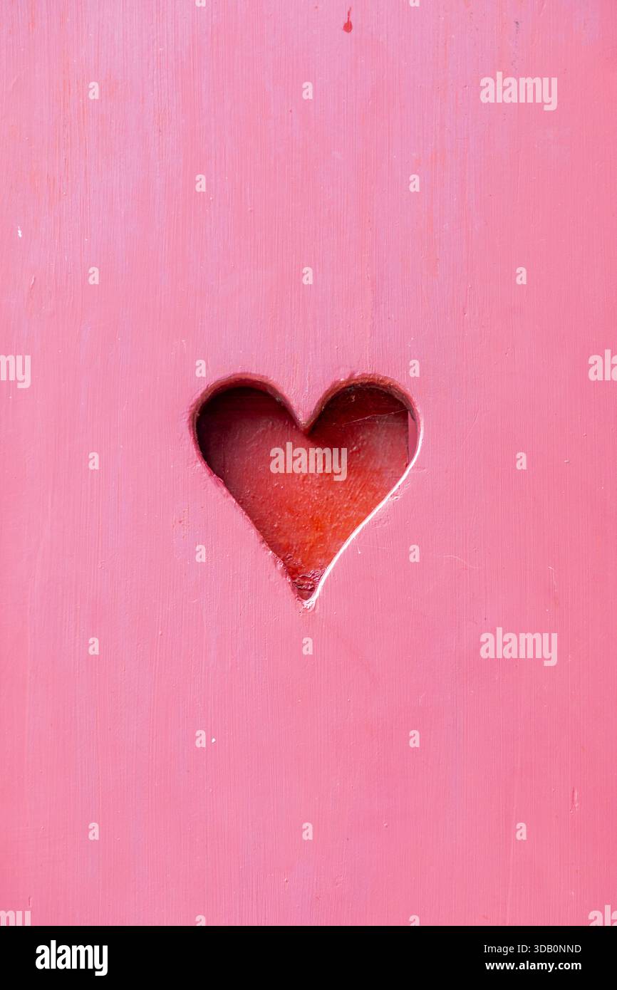 Una superficie in legno rosa brillante presenta una delicata fessura a forma di cuore che rivela un caldo interno rosso. Questa immagine trasmette amore, tenerezza e accogliente rom Foto Stock