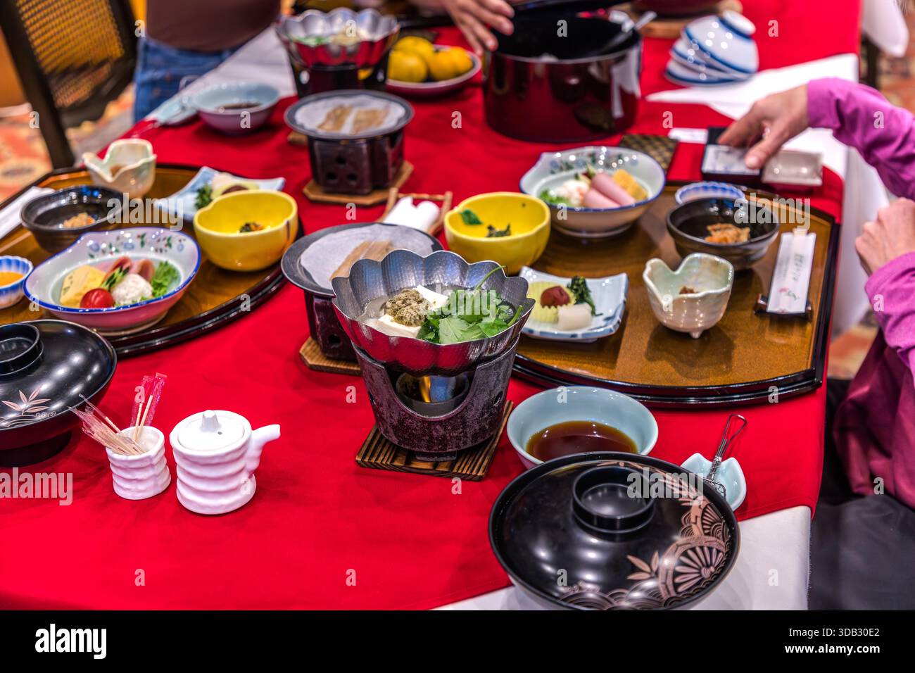Un vassoio per la colazione giapponese riccamente apparecchiato con diverse piccole ciotole, ciotole di riso giallo e un fornello da tavolo per un piatto di tofu e verdure si trova nella sala da pranzo del Watarase Onsen Hotel Sasayuri nella valle di Hongu. La selezione di pesce, verdure e riso segue ingredienti stagionali e regionali. Hongucho Wataze, Tanabe, Prefettura di Wakayama, Giappone. Foto Stock