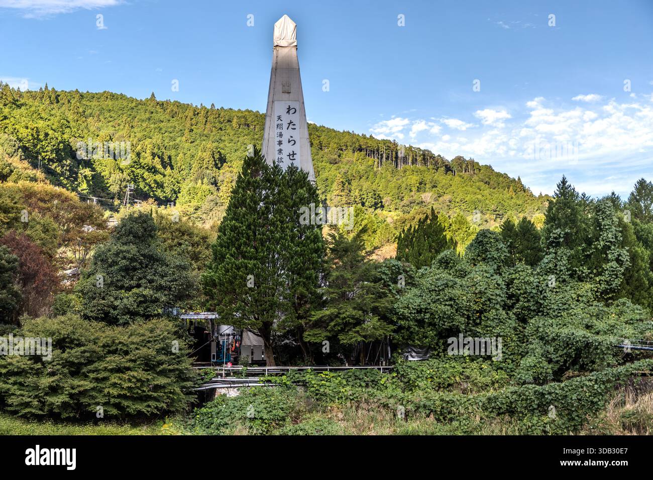 L’obelisco "Watarase" si erge accanto a un ponte sospeso sul fiume Yomura, con l’hotel Watarase Onsen Sasayuri visibile sullo sfondo nella valle di Hongu. Hongucho Wataze, Tanabe, prefettura di Wakayama, Giappone. Foto Stock
