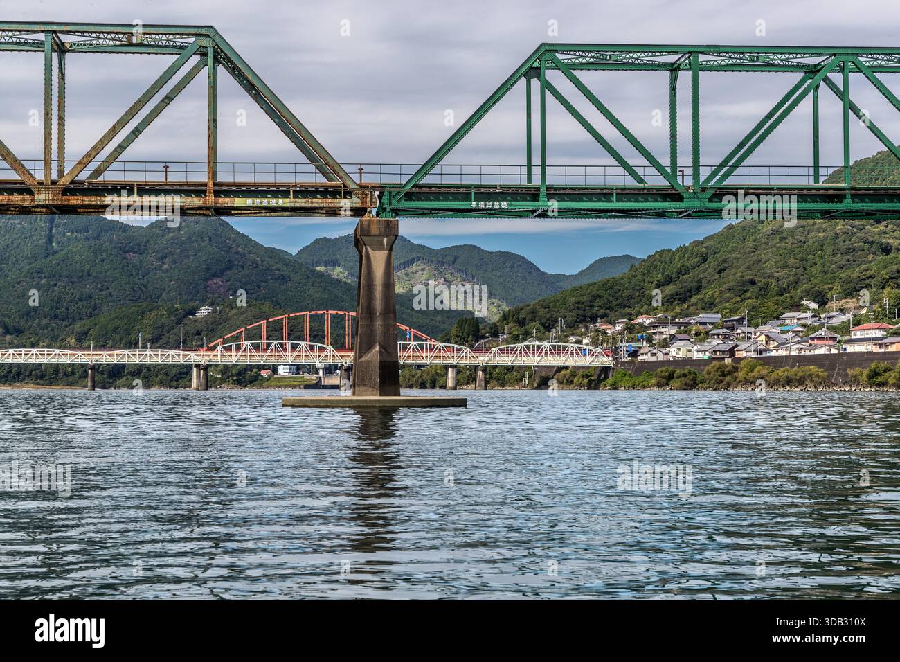 Il ponte ferroviario verde, il ponte ad arco rosso e il ponte stradale bianco attraversano il fiume Kumano vicino a Shingū, con una fila di case sul fiume visibili sullo sfondo. Il percorso in barca segue la via navigabile storica su cui gli imperatori giapponesi e i nobili di corte viaggiavano durante il periodo Heian da Kumano Hongū Taisha a Kumano Hayatama Taisha. Foto Stock