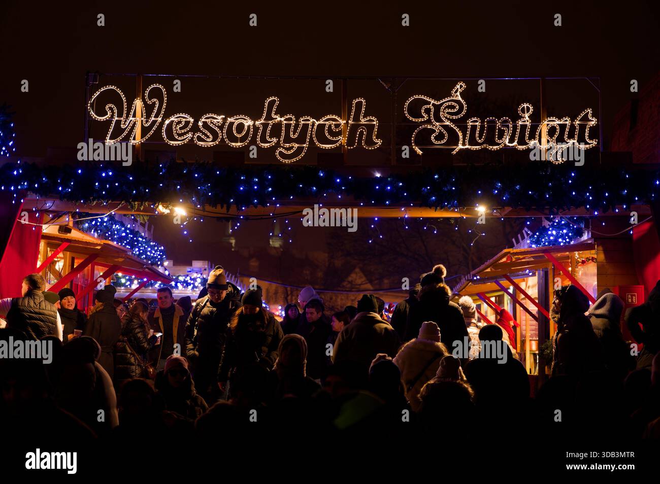 Affollato ingresso al mercato di Natale di notte con luci festive e decorazioni natalizie, atmosfera invernale e gente che fa shopping. Foto Stock