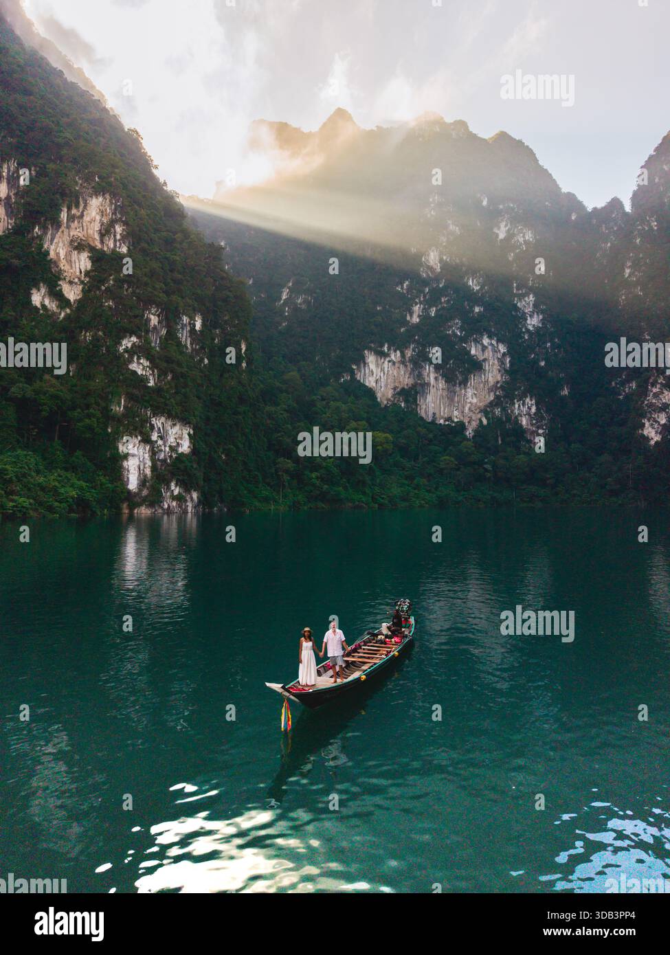 Due viaggiatori si godranno un tranquillo giro su una barca tradizionale in mezzo allo splendido paesaggio del lago Cheow LAN. Khao Sok, Thailandia, una coppia di fronte a una barca a coda lunga all'alba Foto Stock