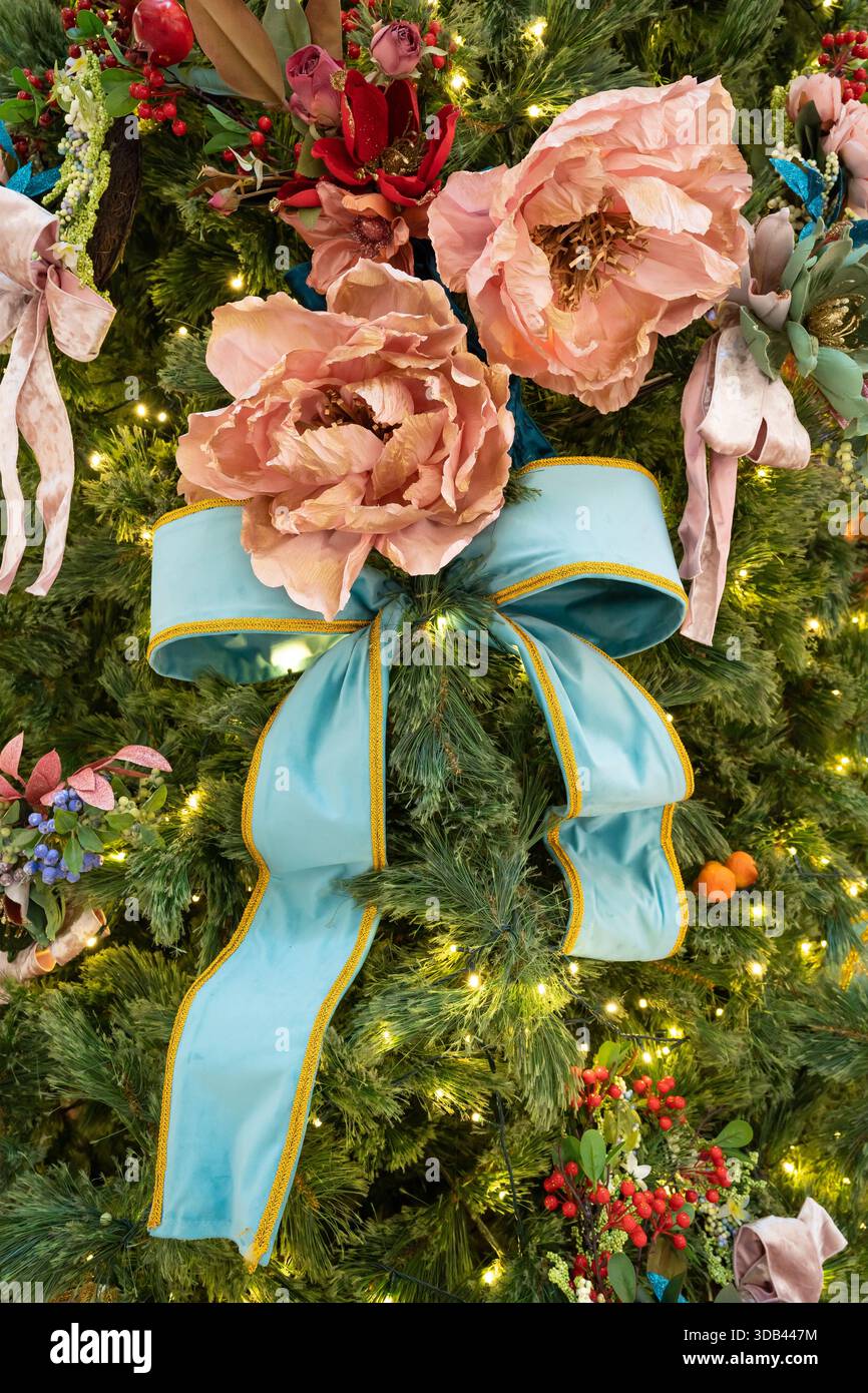 Un festoso albero di Natale adornato da vegetazione lussureggiante, rose rosa tenui e un audace fiocco turchese. Foto Stock