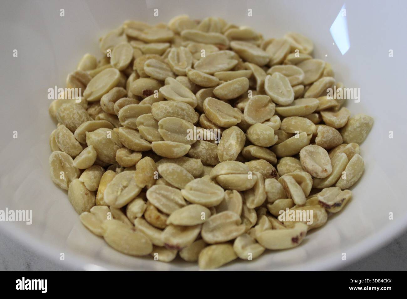 Una ciotola contiene una quantità di chicchi di arachidi crudi. Le arachidi sono di colore chiaro e pulite, pronte per la cottura o per gli spuntini. La scena è ambientata in una cucina Foto Stock