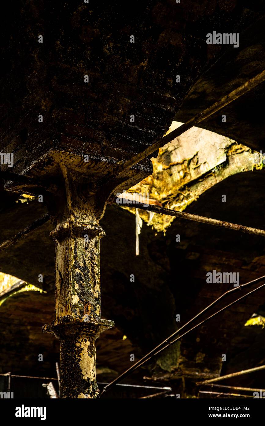 Colonna in ghisa arrugginita sotto il soffitto in mattoni a volta in un interno di fabbrica decaduto Foto Stock