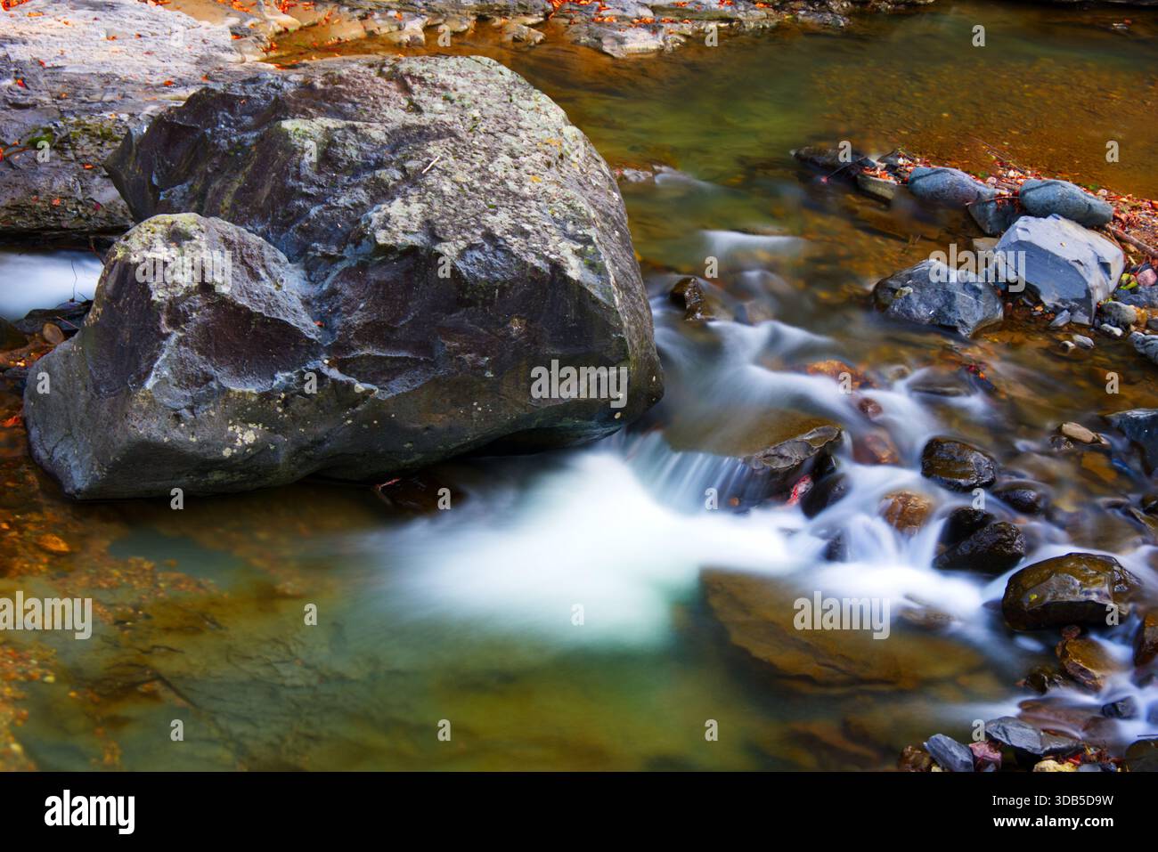 Flusso astratto: Lunga esposizione dell'acqua del fiume intorno alle masse Una fotografia ad alto angolo, primo piano e lunga esposizione che cattura il movimento artistico del fiume Foto Stock