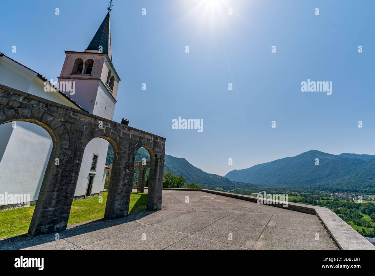 Un solenne memoriale militare nella valle del Soca slovena, incorniciato da strutture ad arco in pietra e vette torreggianti, che evocano pace e riflessi sotto la luce del sole Foto Stock