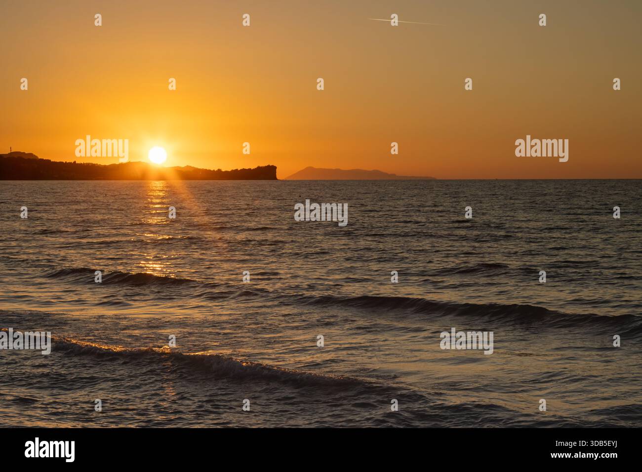 Mare Ionio con onde durante una tarda serata estiva. Cape Roda sullo sfondo. Cielo arancione al tramonto. A nord dell'isola di Corfù (Korfu), Acharavi Foto Stock