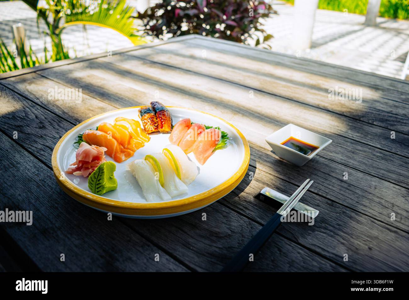 Una selezione di sushi nigiri con salmone, tonno e pesce bianco viene presentata su un piatto di ceramica con zenzero, spicchi di lime e salsa di soia. Bacchette Foto Stock