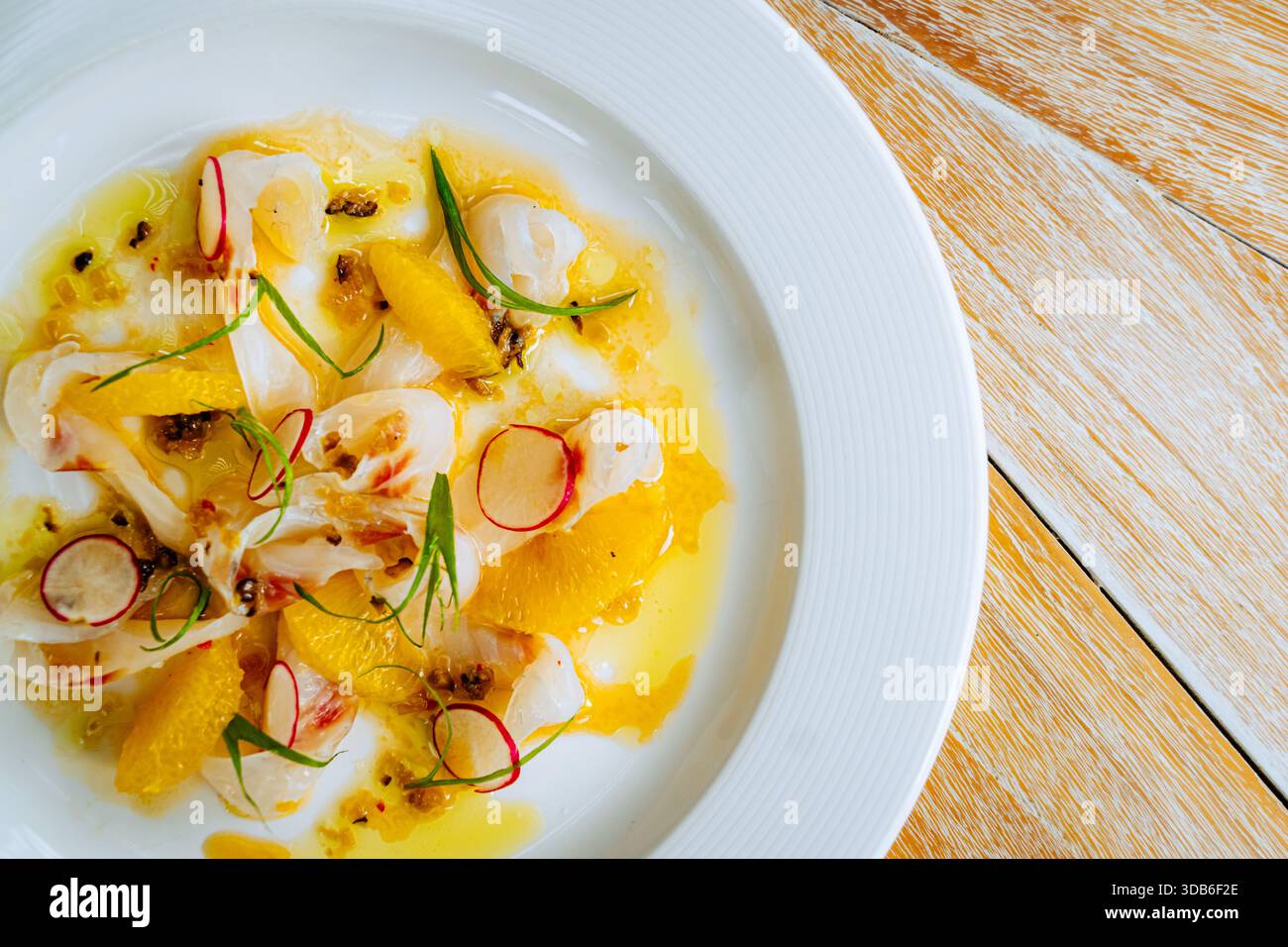 Il ceviche di pesce poggia su un piatto di ceramica con segmenti di agrumi, fette di ravanello e scaglie di cipolla verde. L'olio, la vinaigrette e il pepe fresco aumentano il sapore. Foto Stock