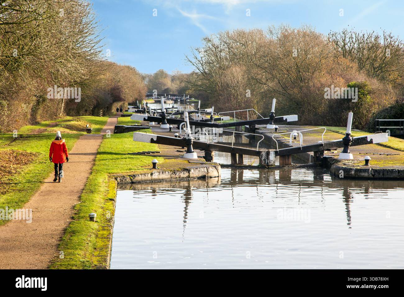 Donna con il cappotto rosso che cammina lungo il sentiero del canale Grand Union al volo delle 21 chiuse di Hatton Locks Warwickshire durante una brillante giornata invernale. Foto Stock