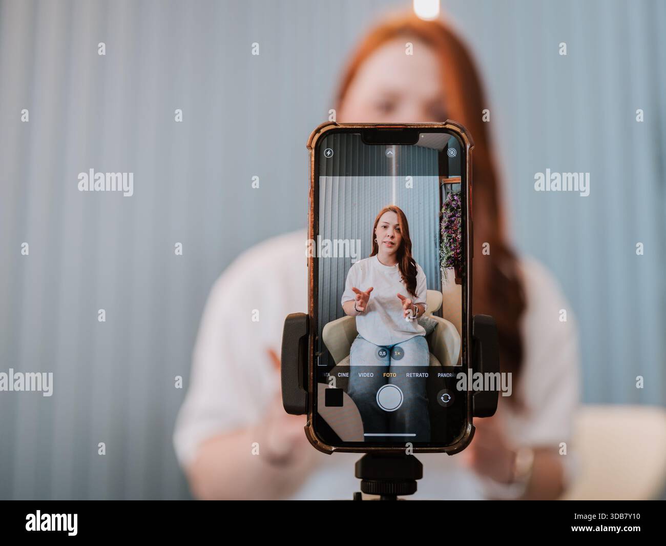 Lo smartphone su treppiede registra una donna che parla con la fotocamera in interni. Creazione di contenuti, influencer marketing e produzione di video. Foto Stock